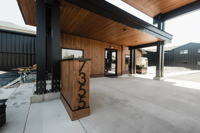 Riverstone address monument sign at modern cedar-and-steel entrance under a warm wood-paneled canopy