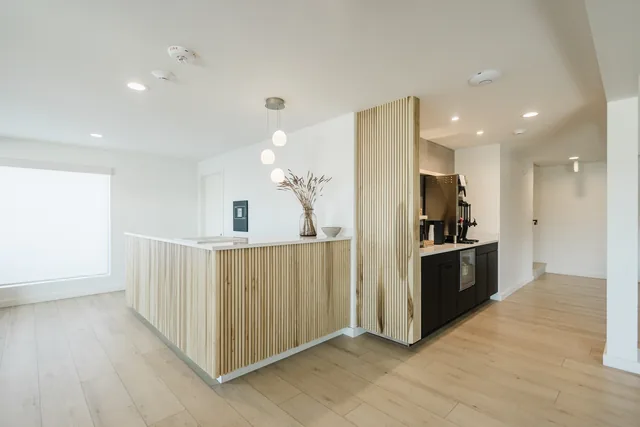 Riverstone front desk with slatted light-wood facade, globe pendant trio, and complimentary coffee bar beyond