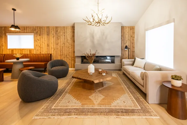 Sun-filled Riverstone lobby lounge with antler chandelier, stone fireplace, bouclé chairs, and warm wood accent wall