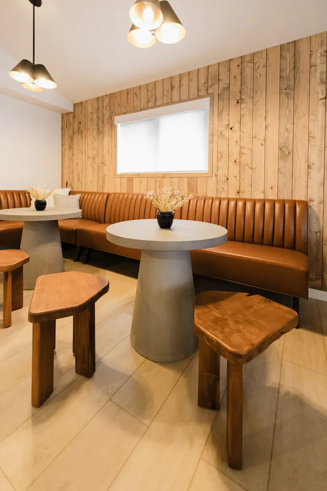 Intimate banquette nook with channel-tufted cognac leather, concrete pedestal table, and reclaimed wood plank wall