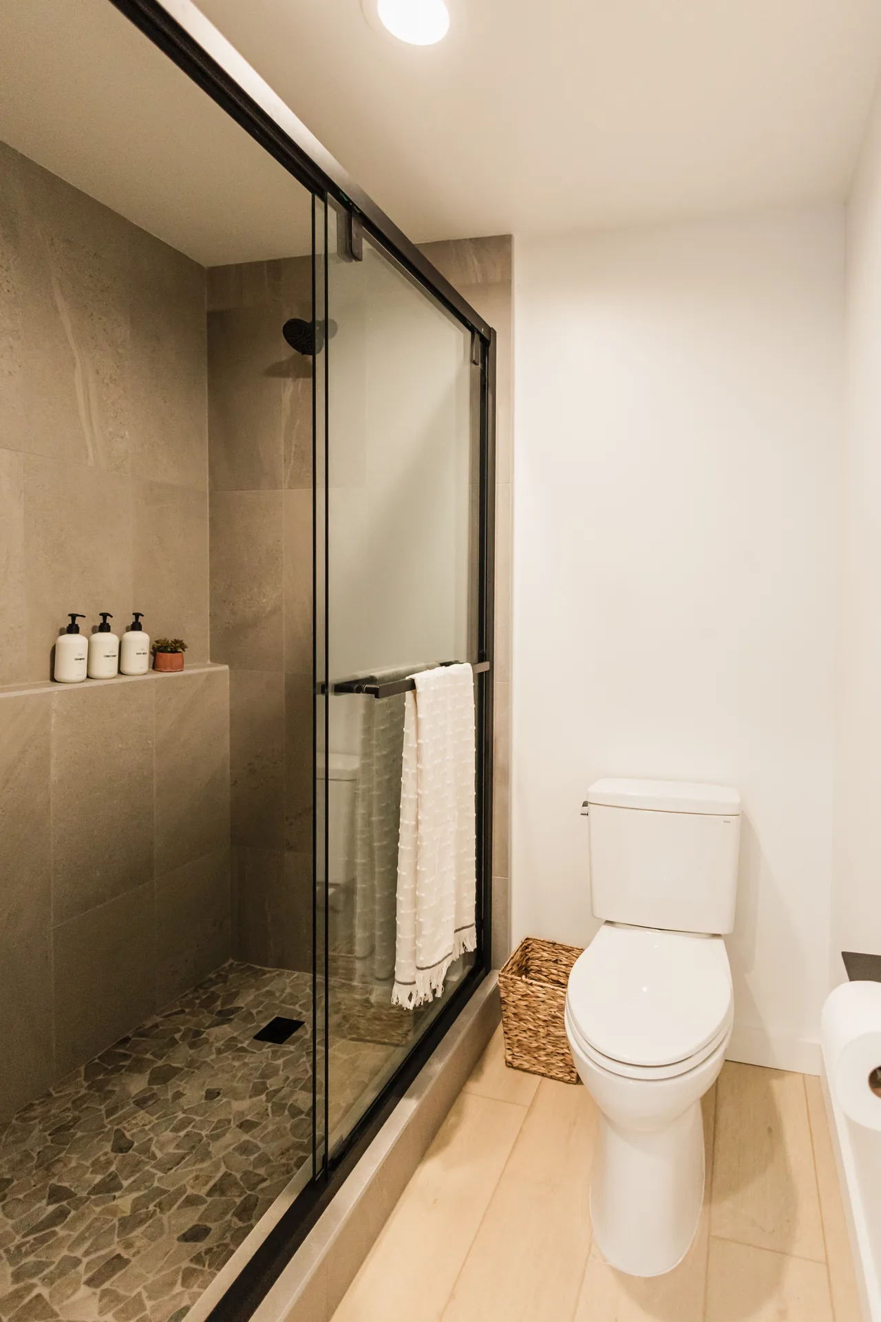 Walk-in shower with river-pebble floor, floor-to-ceiling tile, glass enclosure, and white bath amenities on ledge