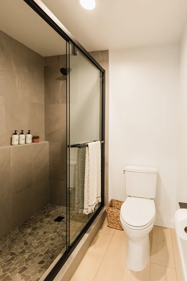 Walk-in shower with river-pebble floor, floor-to-ceiling tile, glass enclosure, and white bath amenities on ledge