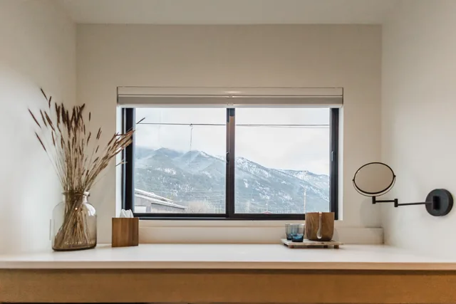Vanity ledge with dried grass vase and mirror framing a snow-dusted mountain view through a black-frame window