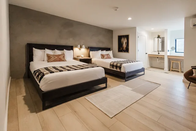 Bright double-queen room with dark plaster accent wall, black-frame beds, plaid runners, and mountain-view window