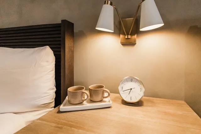 Bedside nightstand with paired ceramic mugs, brass double sconce glowing warm against a textured plaster wall