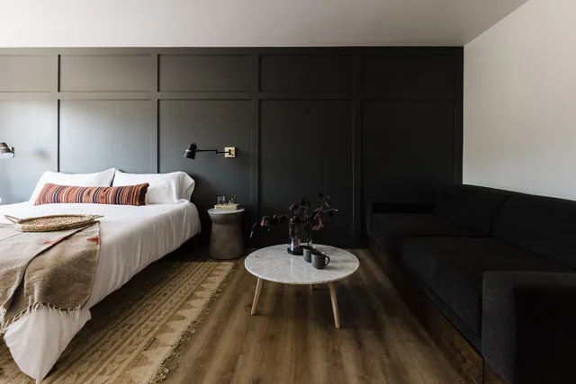 Boutique king suite with dark paneled accent wall, marble coffee table, and earthy woven rug