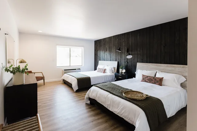 Bright double queen room with charcoal shiplap accent wall, two crisp white beds, brass sconces, and warm wood floors
