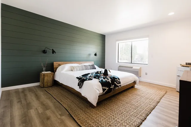 King bedroom with forest-green shiplap accent wall, reclaimed-wood platform bed, white duvet, and jute rug