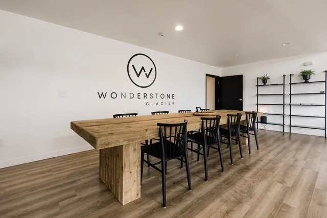 Communal wooden farm table with black Windsor chairs beneath the Wonderstone Glacier logo wall and open industrial shelving