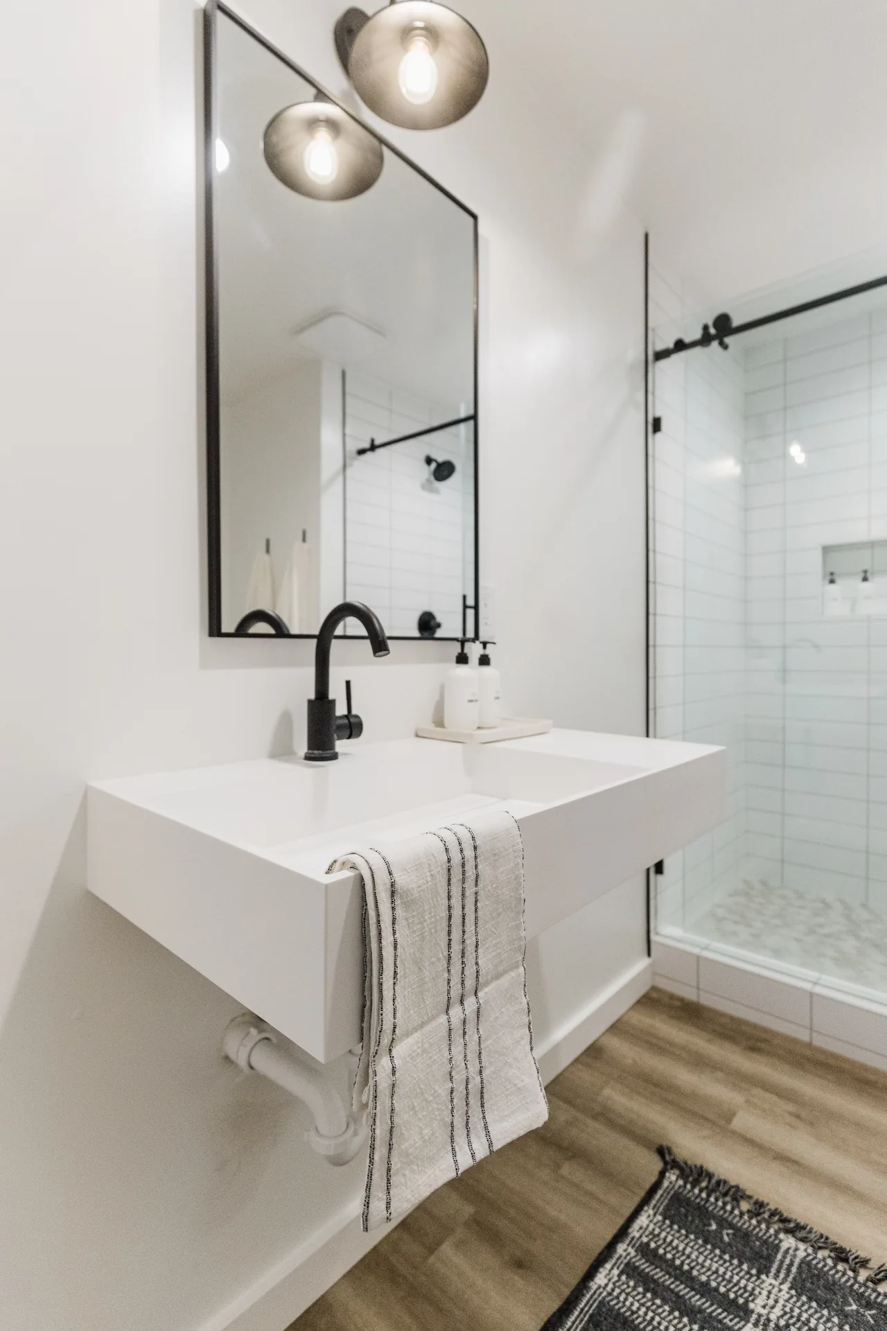 Clean white bathroom with floating vanity, matte black faucet, globe pendant lights, and frameless glass shower