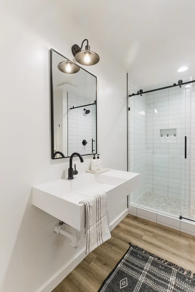 Suite bathroom with floating white vanity, matte-black fixtures, barn-door glass shower, and woven rug