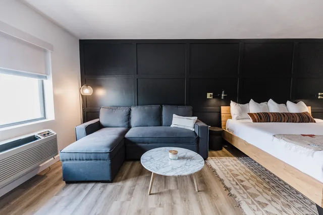 Suite sitting area with navy sectional sofa, marble coffee table, and king bed against black accent wall
